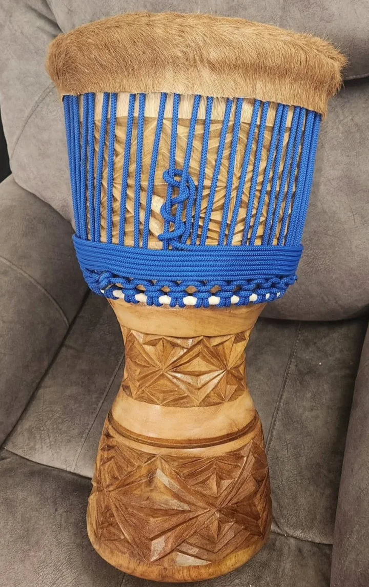 Djembe with bright blue rope, tan hair-on rim, and geometric star carving on a pale wooden shell