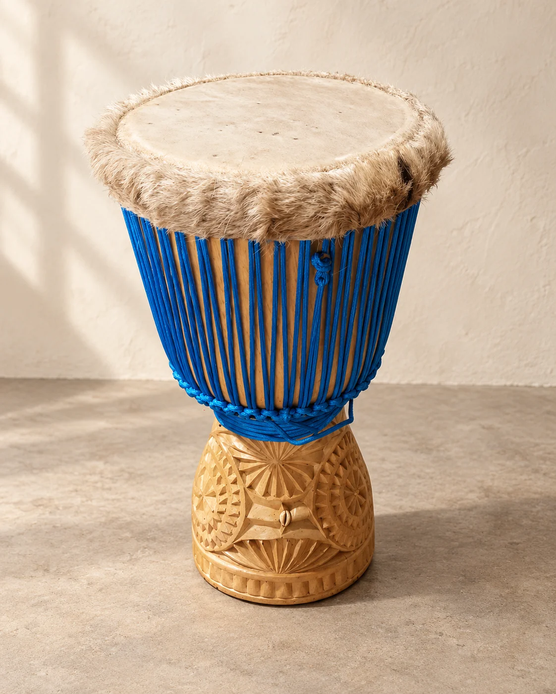 Light carved-wood djembe with cobalt blue rope and radial geometric details