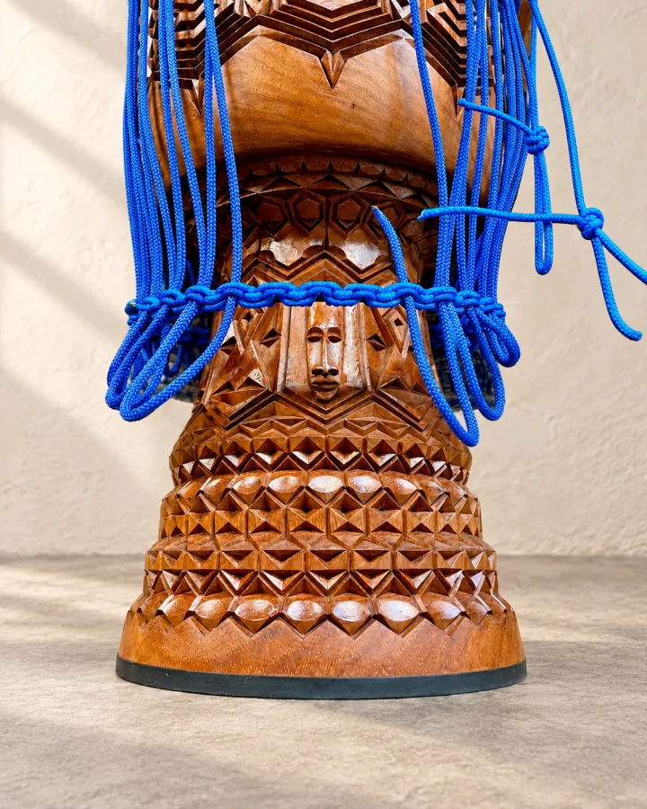 Close-up of a carved face and layered geometric bands on a warm wood djembe with blue rope